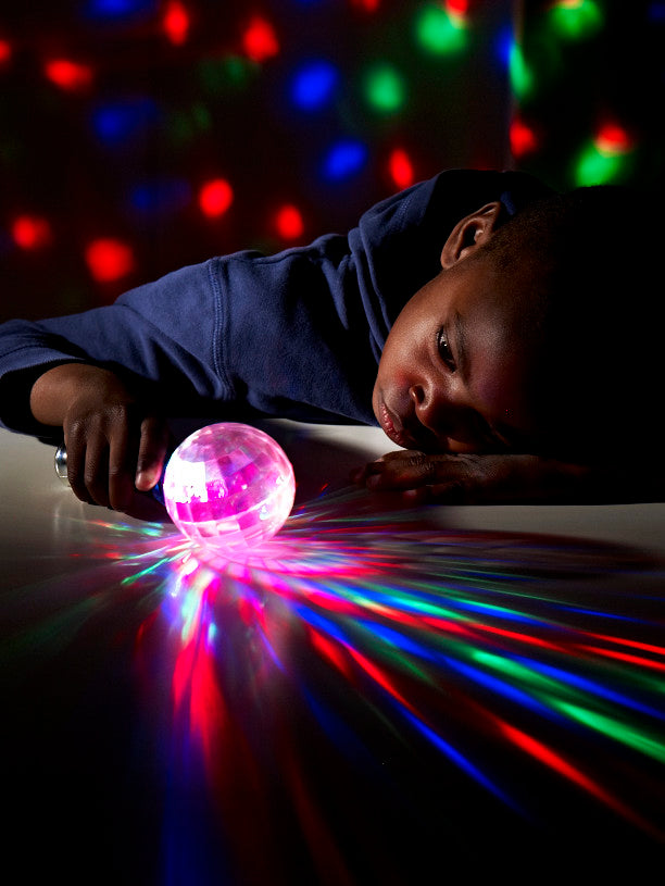 A child rests their head on a table, watching a light-up ball glow in the dark